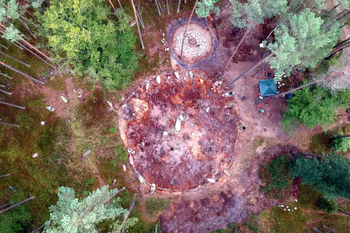 Starożytne kamienne kręgi w lesie, otoczone drzewami. Widać archeologów przy pracy i zielony namiot.