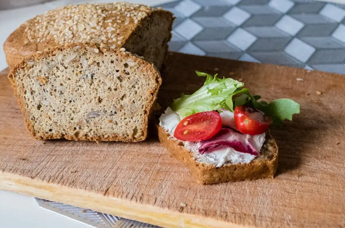 Keto chleb majonezowy przepis: kromka z serkiem, pomidorkami i sałatą obok bochenka z ziarnami.