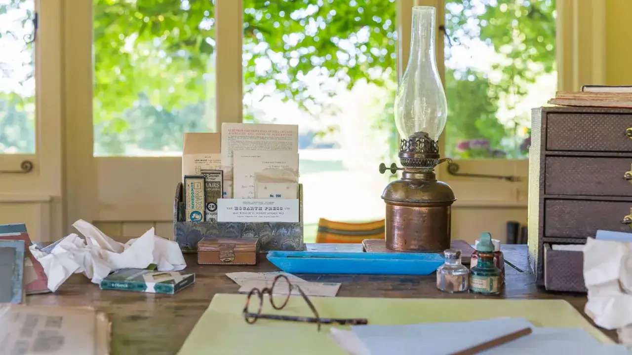 Scrivania con lampada a olio, occhiali e documenti, evocando l'atmosfera di Virginia Woolf e della Hogarth Press.