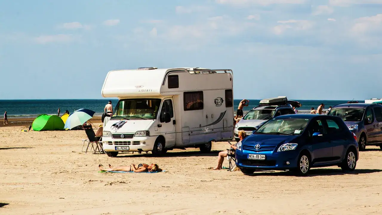 Solig stranddag p&aring; Jylland med husbil, bilar, t&auml;lt och solbadare.