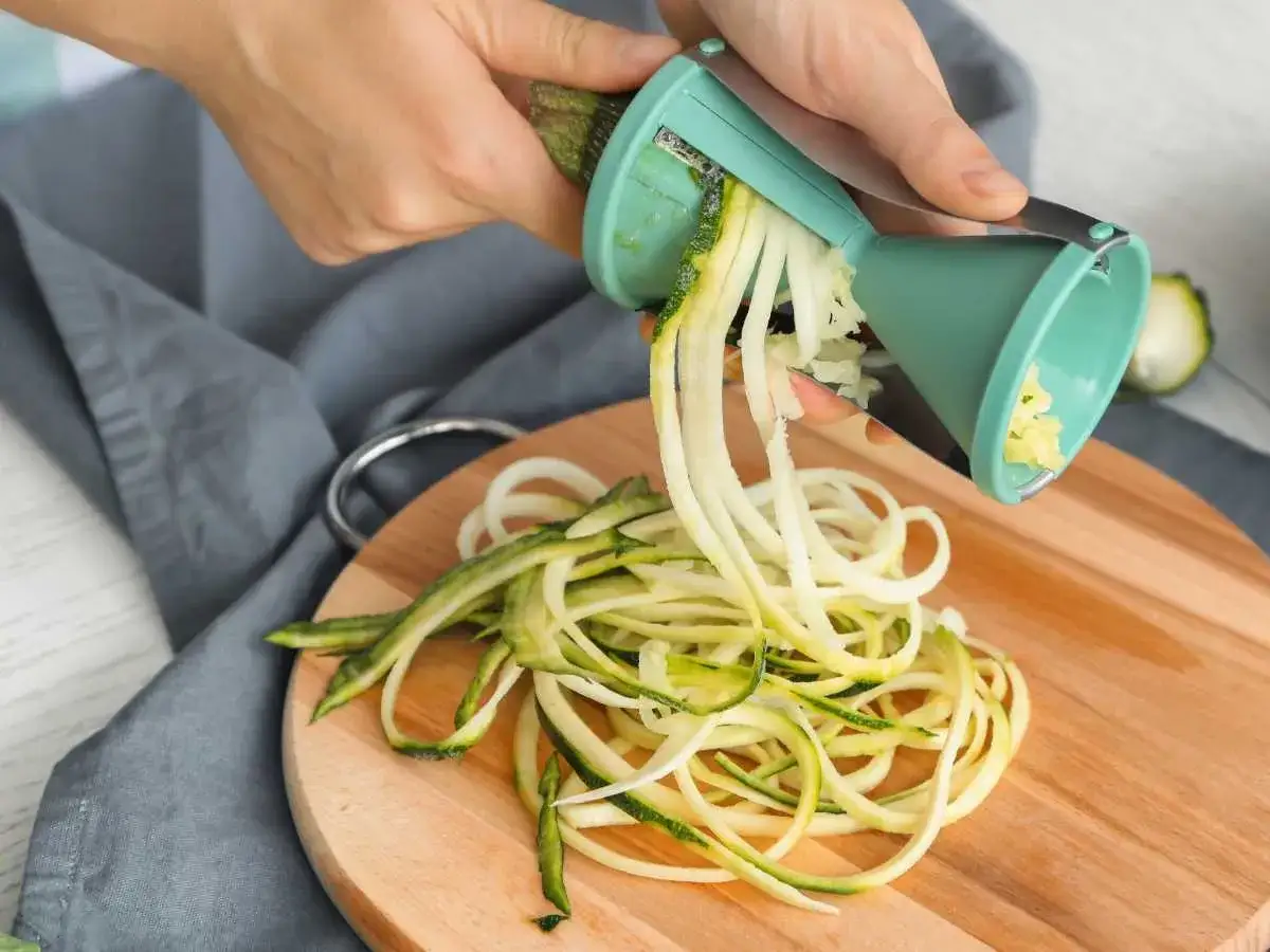 Manos creando tallarines de calabac&iacute;n con un espiralizador. Una forma saludable y divertida de preparar tus verduras.