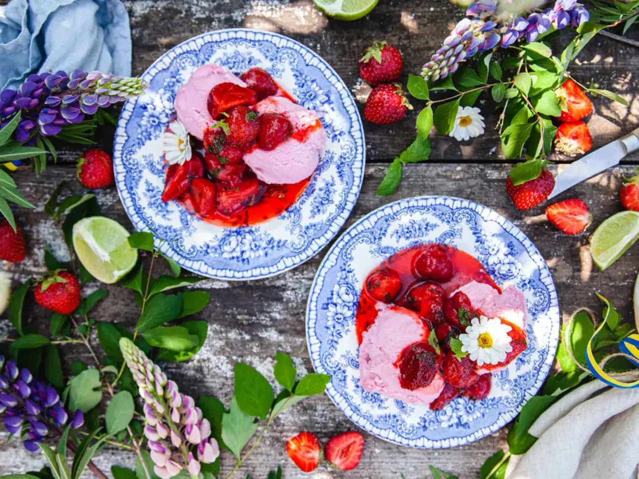 Två tallrikar med rosa rabarbersorbet och färska jordgubbar, omgivna av lupiner och lime. En somrig och svalkande dessert.