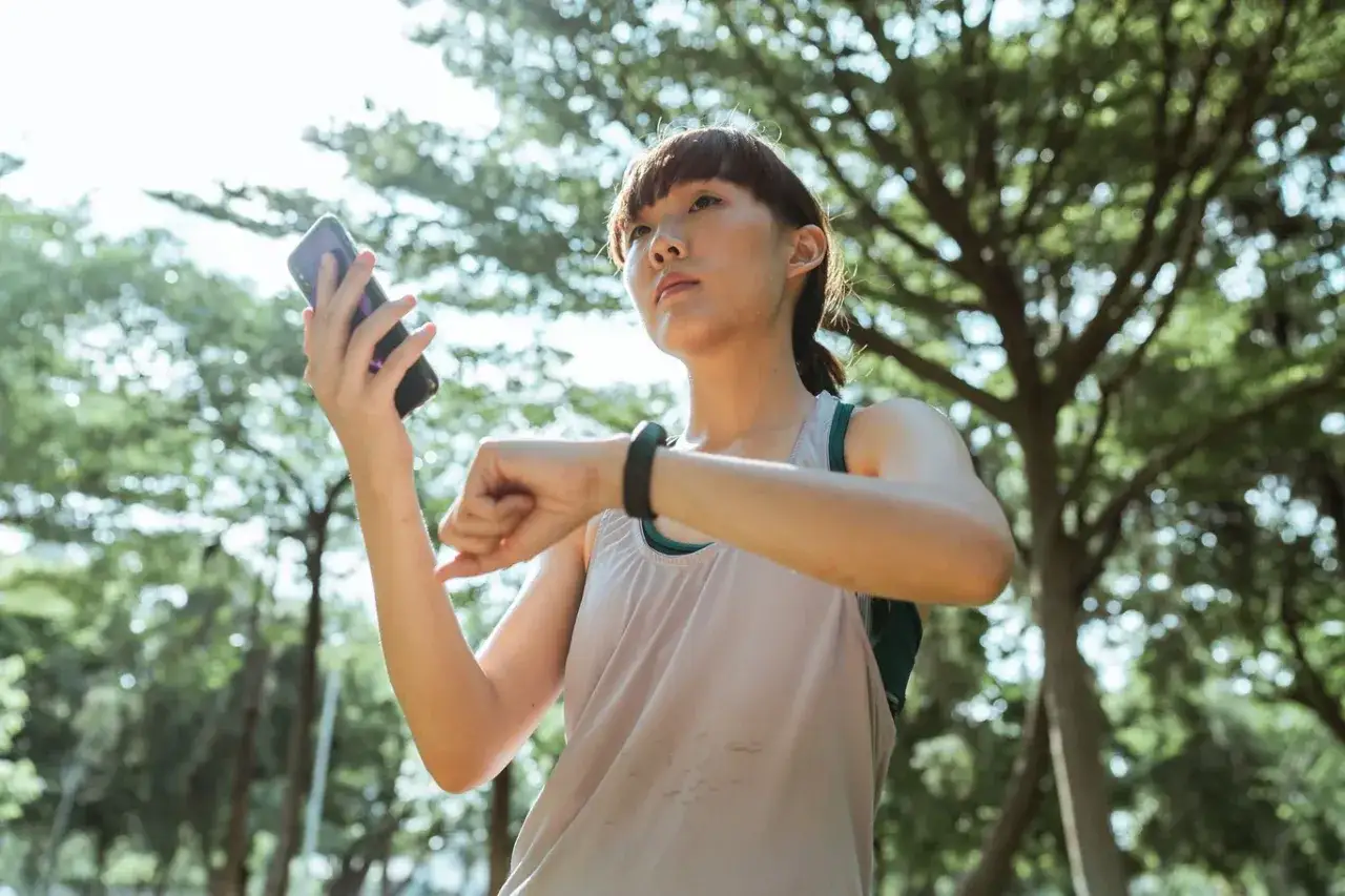 Frau prüft ihre Fitnessuhr im Park, um sicherzustellen, dass sie ihre 10.000 Schritte am Tag erreicht.