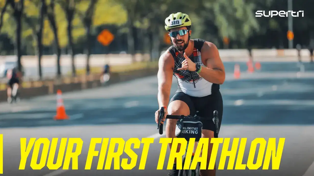 A smiling man in a cycling helmet and sunglasses gives a shaka sign while riding a bike, ready for his first triathlon.