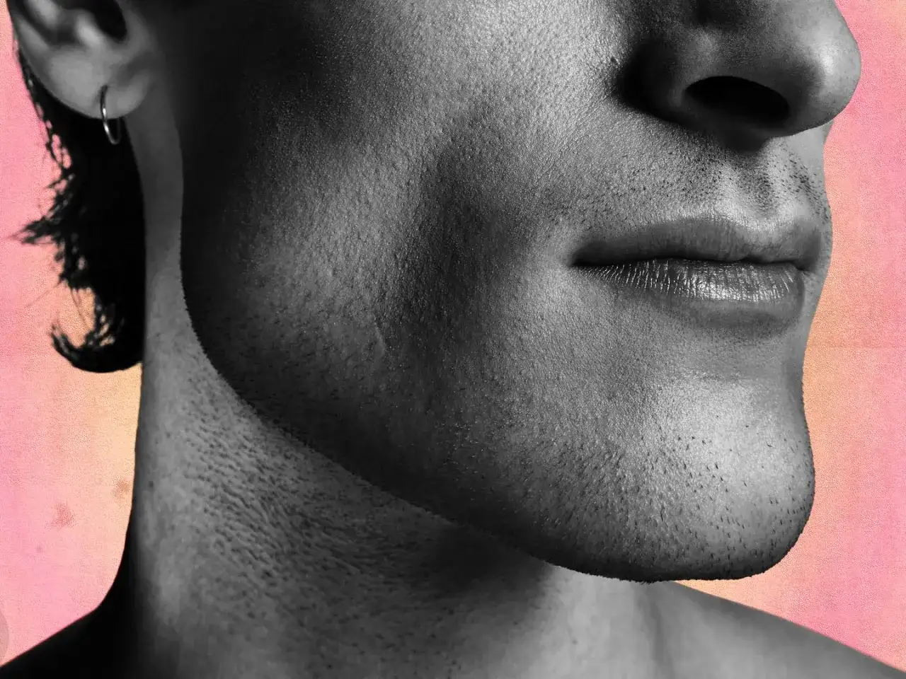 Gros plan sur le visage d'un homme, mettant en valeur sa mâchoire définie et sa barbe naissante. La ligne en V de son menton est accentuée par un éclairage dramatique.
