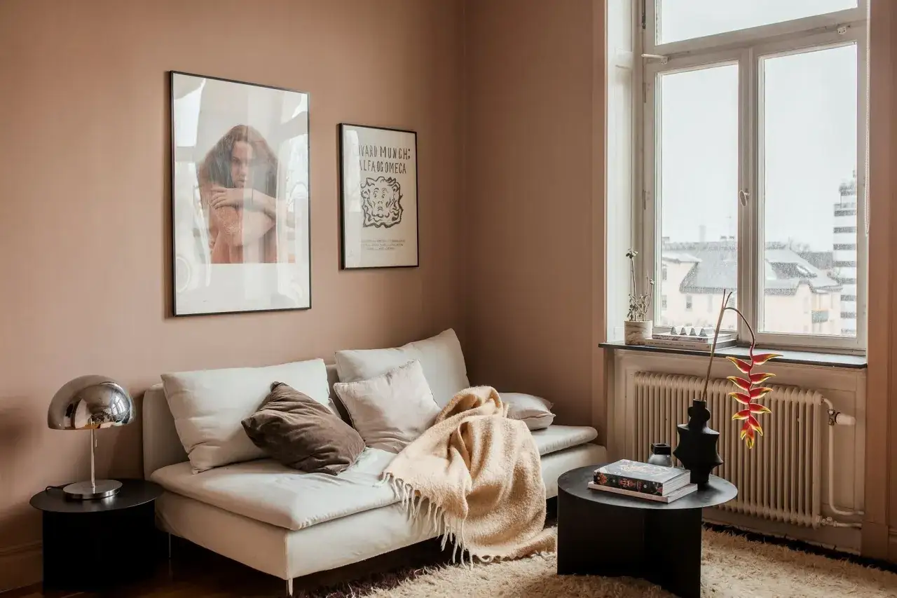 Soggiorno accogliente con divano bianco, coperta color pesca e pareti color rosa antico.