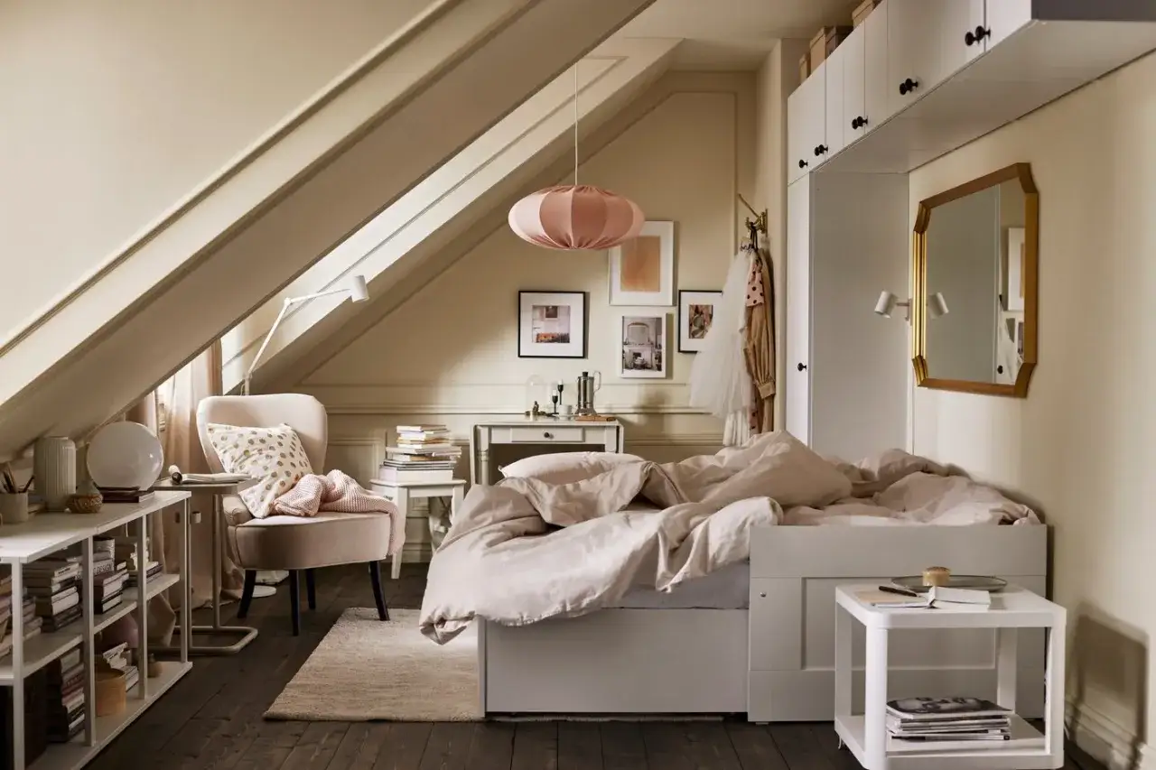 Chambre mansard&eacute;e d'un cot&eacute;, avec un lit douillet, un fauteuil confortable et une &eacute;tag&egrave;re remplie de livres.