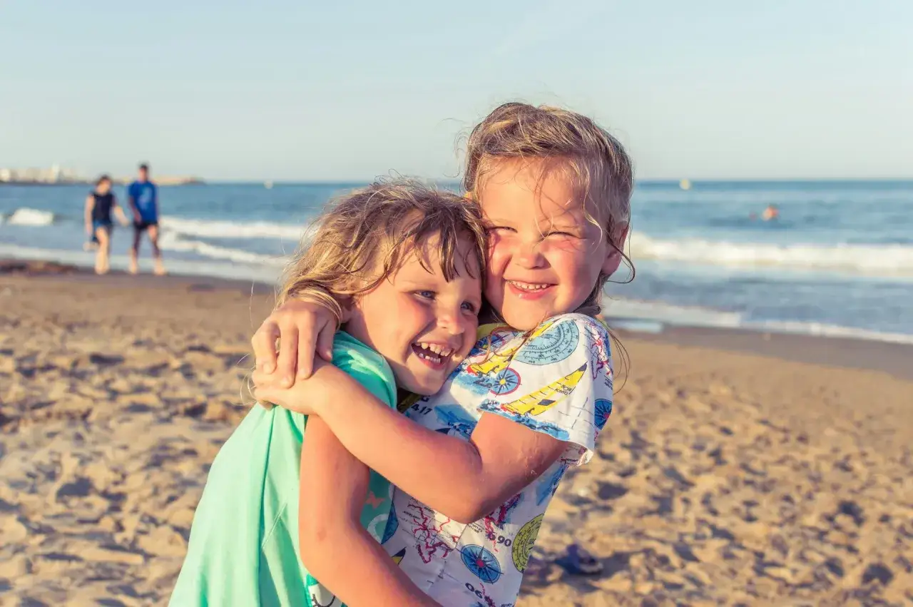 Dwie dziewczynki przytulają się na plaży. Idealne miejsce, gdzie na wakacje z niemowlakiem, bo plaża jest piaszczysta i bezpieczna.