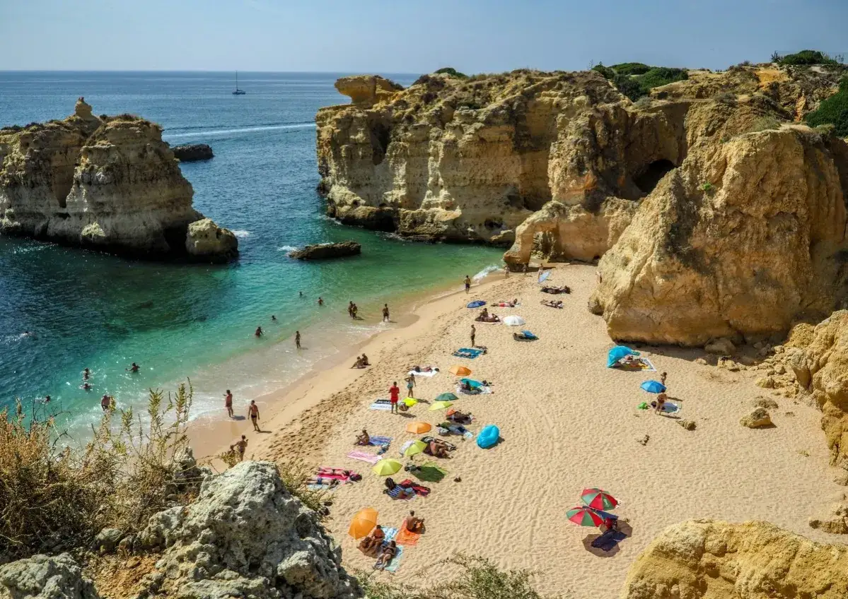Słoneczna Portugalia w lipcu. Plażyści odpoczywają na piaszczystej plaży, kąpią się w turkusowej wodzie, podziwiając skaliste klify.