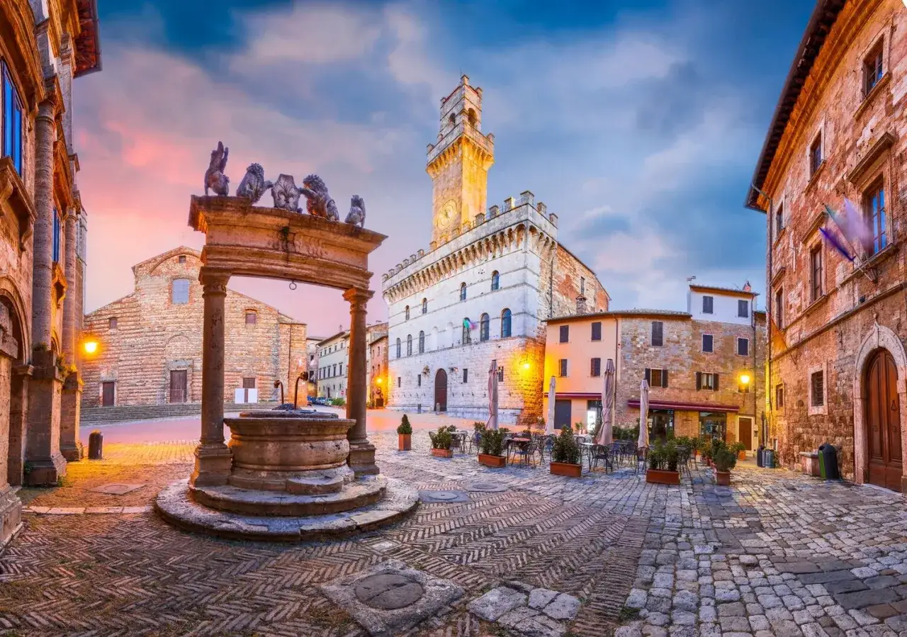 Piazza medievale con pozzo, palazzo comunale e chiesa. Un angolo suggestivo di Arezzo e dintorni al tramonto.