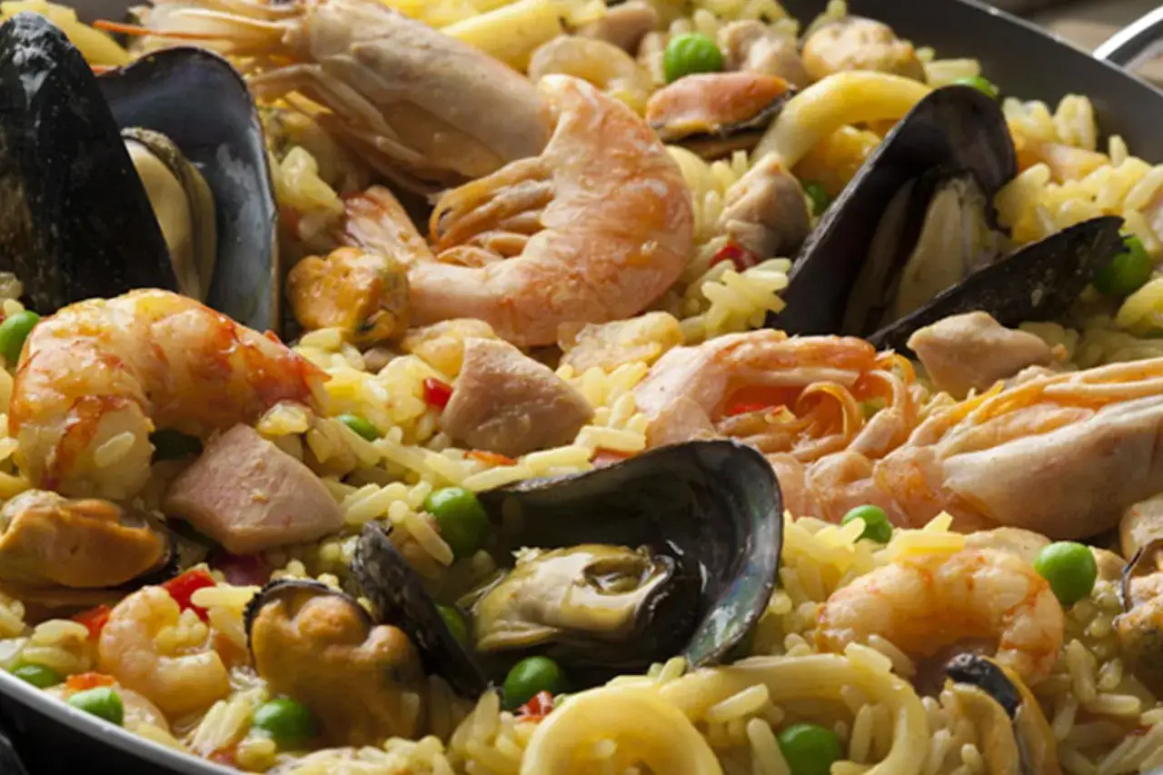 Arroz con pollo y marisco, un festín de gambas, mejillones y trozos de pollo sobre arroz amarillo, adornado con guisantes verdes.