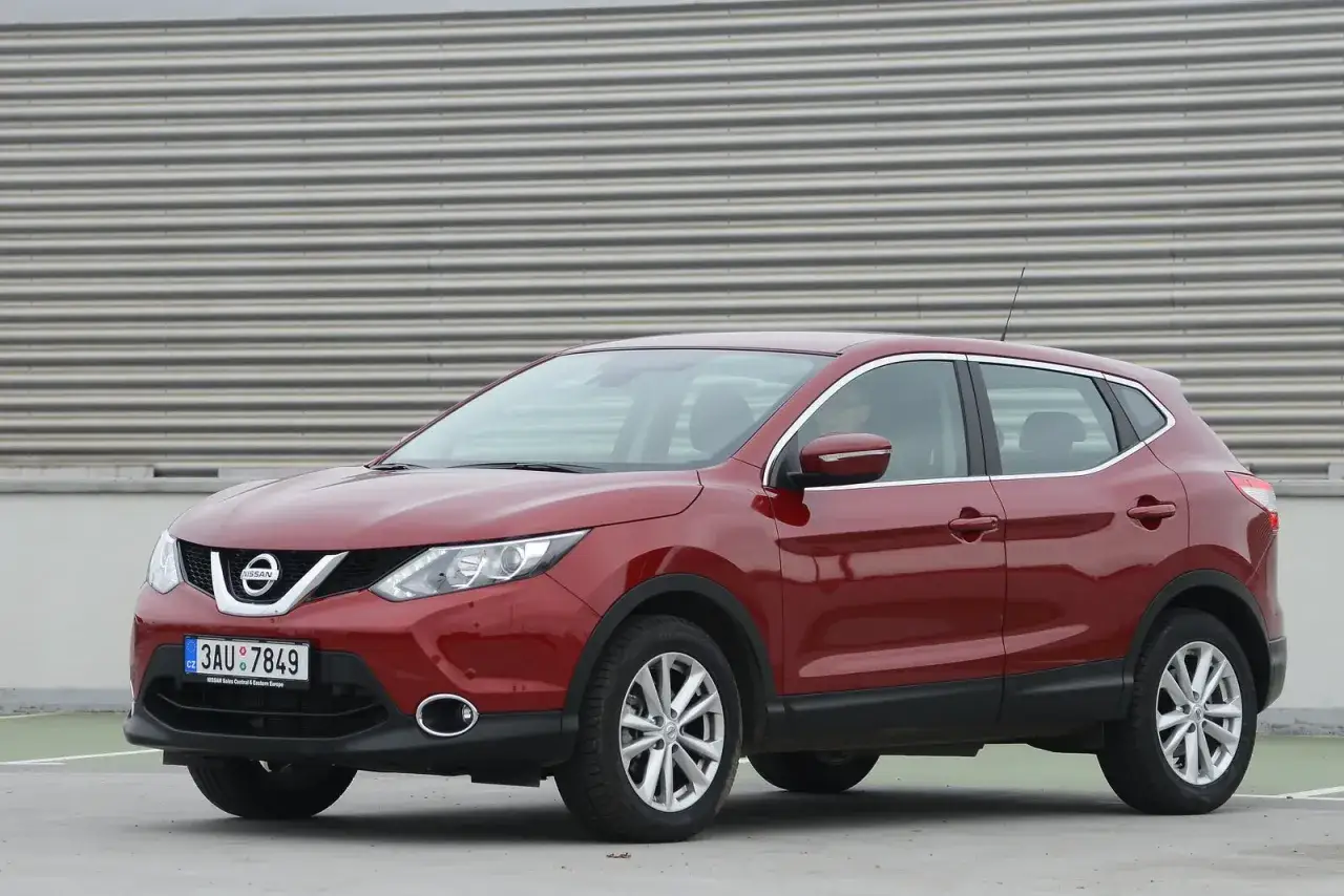 Czerwony Nissan Qashqai J11, widok z boku. Wykaz żarówek jest częścią jego oświetlenia.