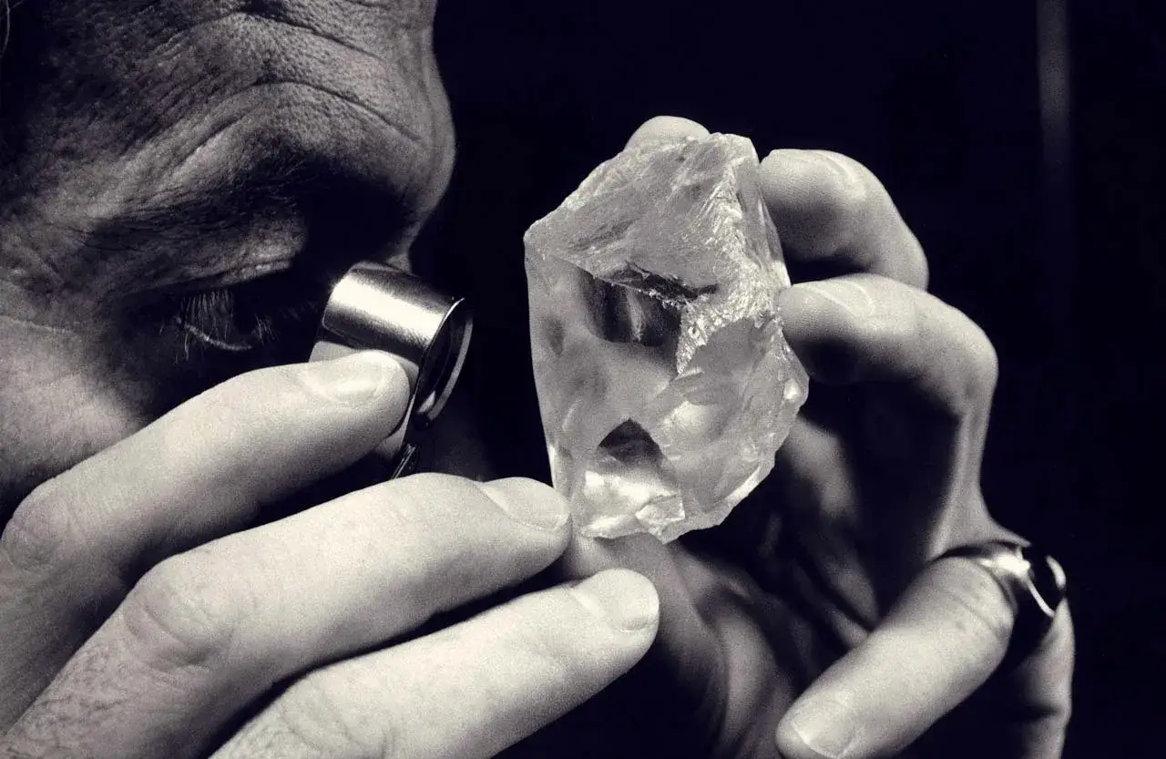 Un joyero examina un gran diamante tallado con una lupa, evaluando su pureza y potencial.