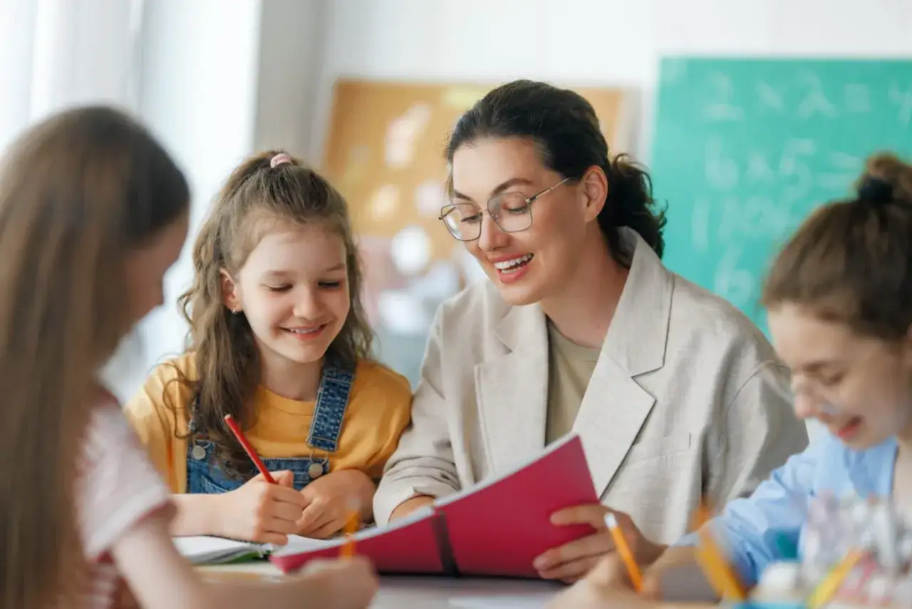 Lehrerin erklärt einer Gruppe von schüler im unterricht eine aufgabe. Sie lächeln und arbeiten konzentriert.