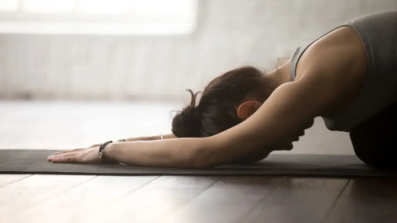 Kobieta w pozycji balasana na macie do jogi, zrelaksowana i wyciszona.
