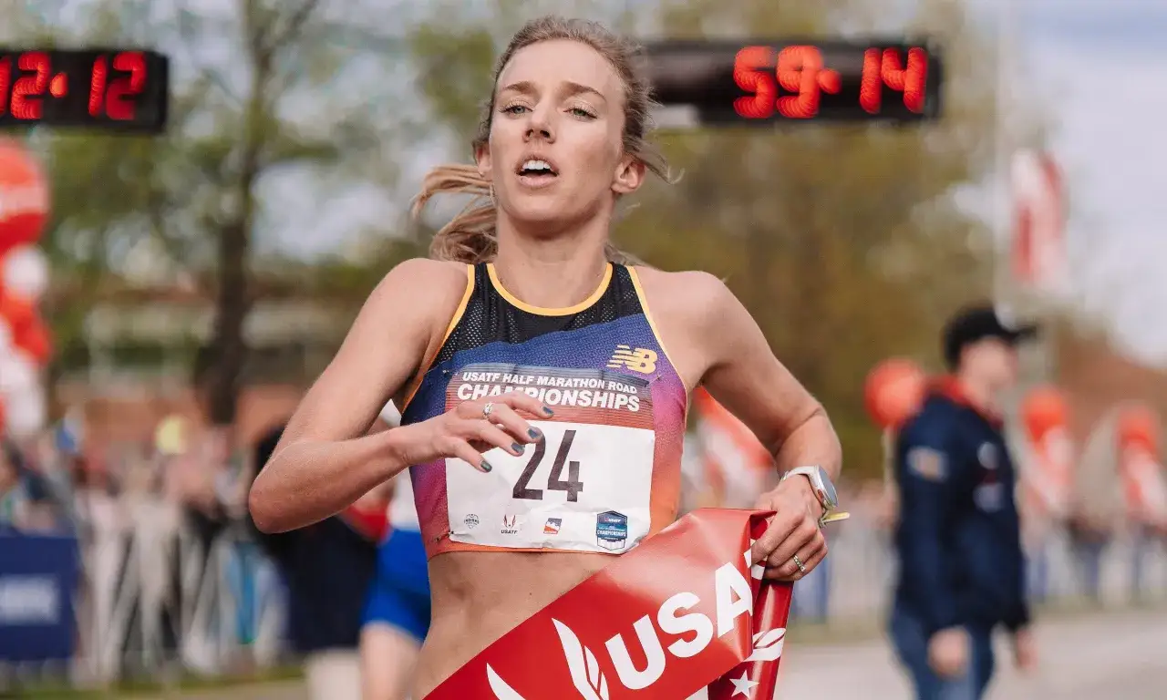Athlète en pleine course, dossard 24, franchissant la ligne d'arrivée d'un semi-marathon. Le chronomètre affiche 59:14.