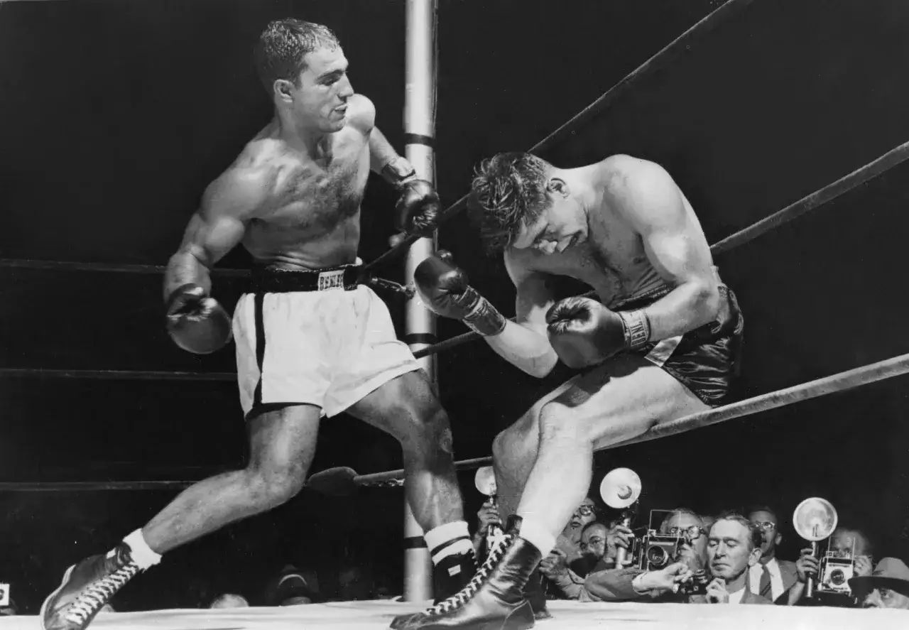 Rocky Marciano, in his signature white shorts, throws a punch during a fight. His intense focus mirrors the dedication of his legendary rocky marciano workout.