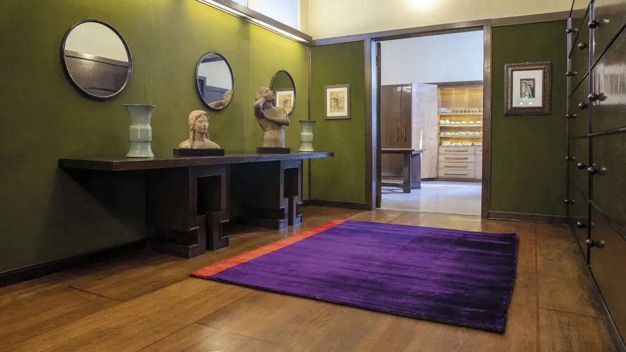 Un corridoio con pareti verdi, sculture, vasi e un tappeto viola acceso, in un audace stile massimalista.