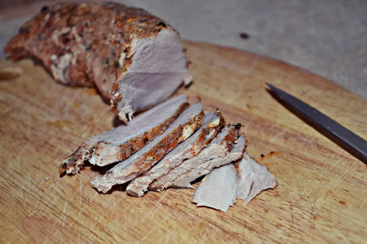 Pokrojona polędwica pieczona na kanapki, przyprawiona i soczysta, leży na desce obok noża.