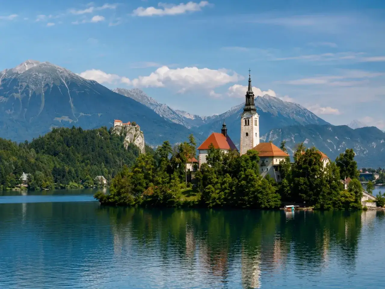 Idyllisches Bild vom Bleder See in Slowenien mit Inselkirche und Burg auf Felsen.