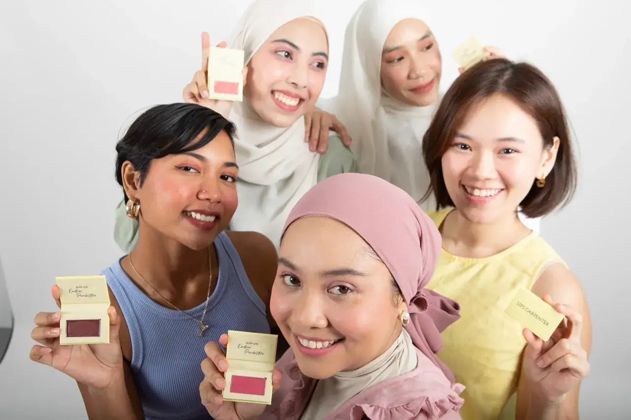 Cinq femmes souriantes tiennent des bo&icirc;tiers de maquillage. L'une d'elles montre un blush couleur blush, promettant des possibilit&eacute;s infinies.