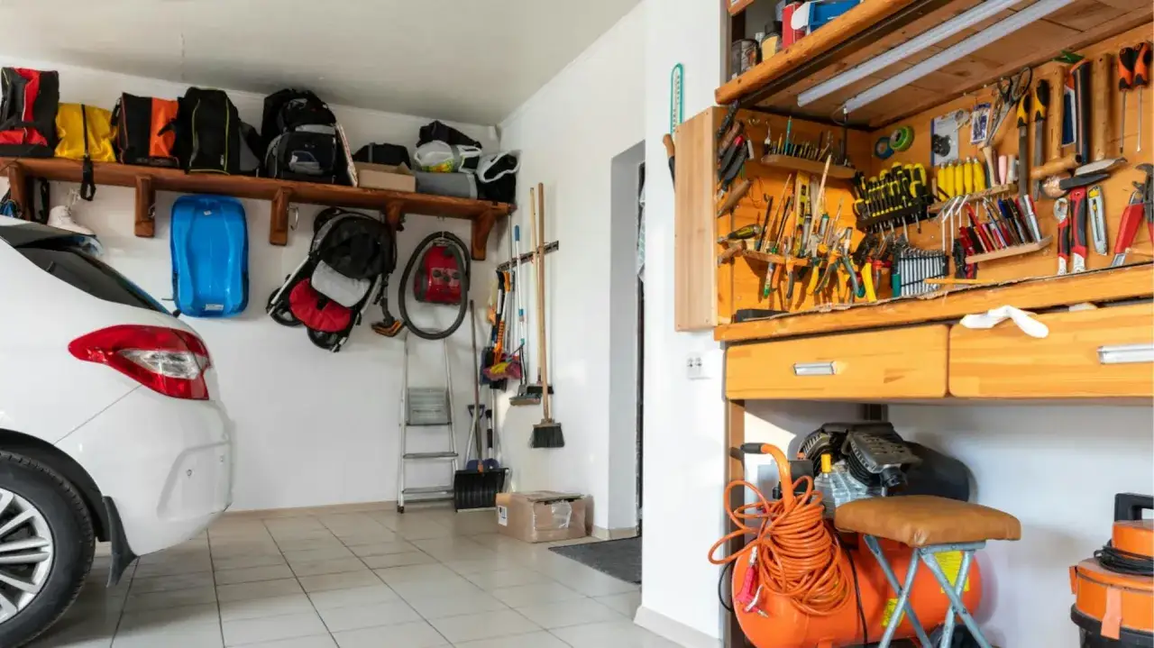 Ordnung in der Garage: Werkstatt einrichten mit Werkzeugwand, Kompressor und Staubsauger. Rucksäcke und ein Kinderwagen hängen an der Wand.