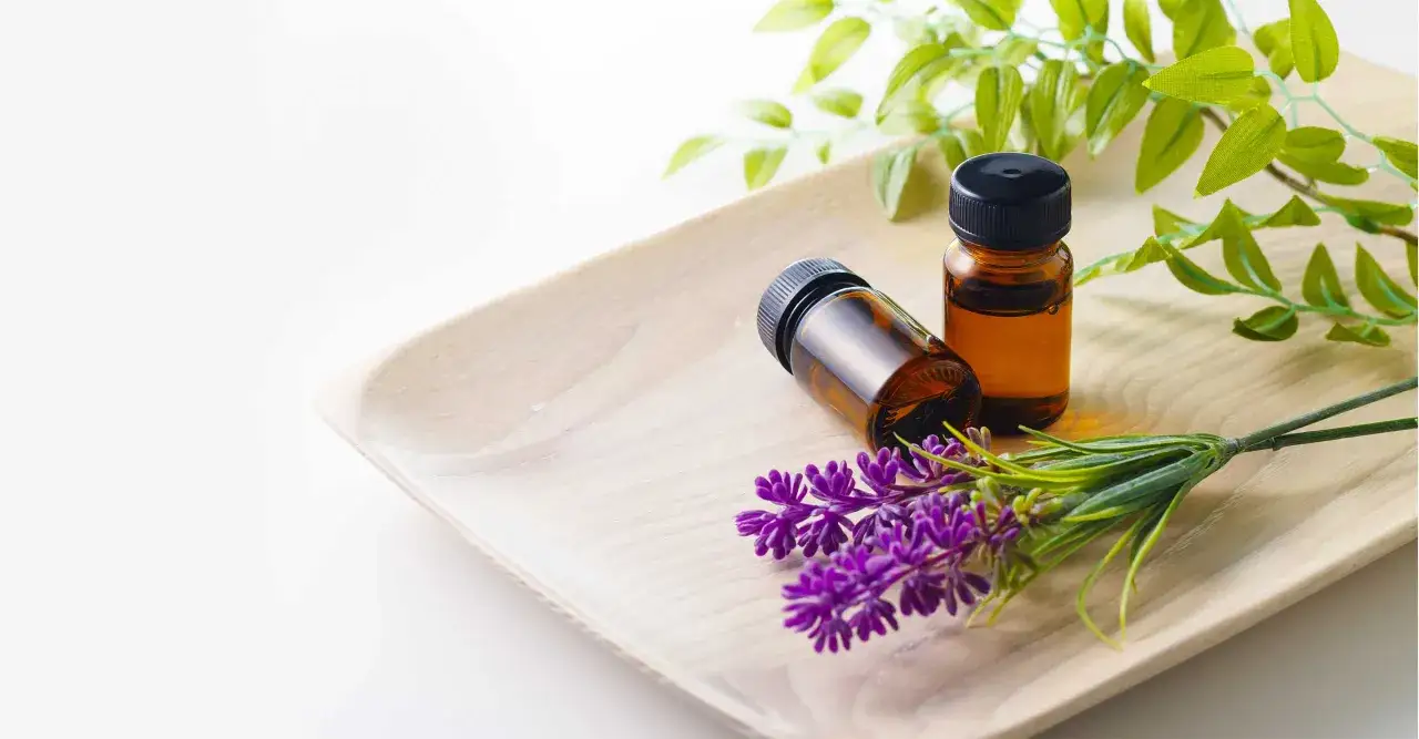 Zwei Fl&auml;schchen mit &auml;therischem &Ouml;l und Lavendelzweige auf einem Holztablett. Die Lavendel wirkung psyche ist beruhigend.