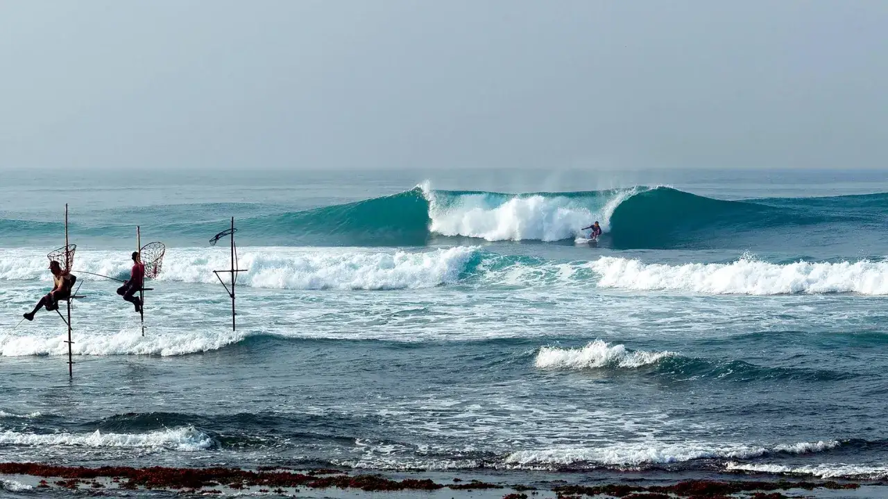 Surfer na fali i rybacy na palach. Idealny czas, kiedy najlepiej lecieć na Sri Lankę, by podziwiać takie widoki.