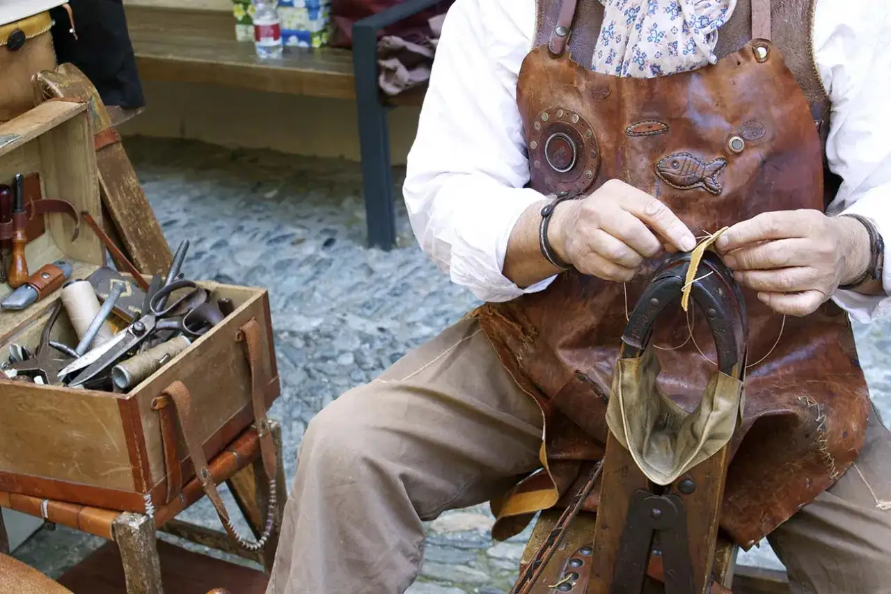 Handwerker n&auml;ht Leder auf dem Bad Wimpfen Zunftmarkt. Werkzeugkasten daneben.