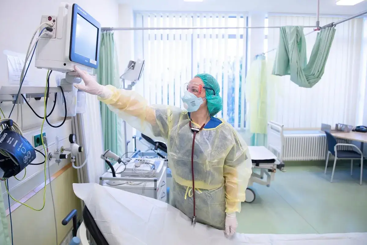 Pielęgniarka w ochronnym stroju dotyka monitora. Wkrótce podwyżki dla pielęgniarek od lipca.