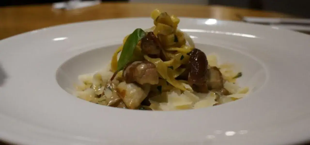 Pyszny, **lekkostrawny makaron** z grzybami i parmezanem, udekorowany listkiem ziół.