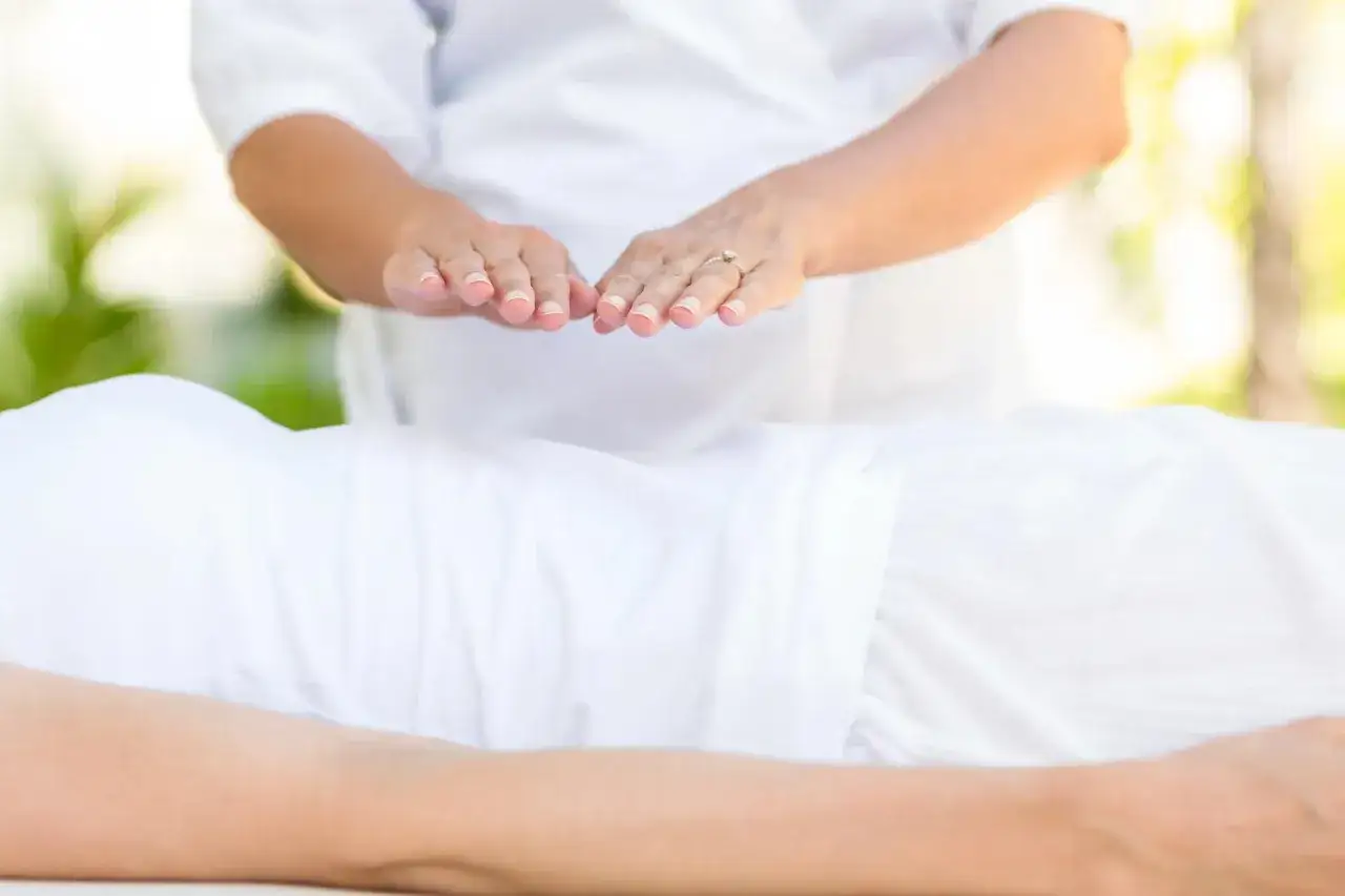 Dłonie terapeuty unoszą się nad ciałem osoby leżącej, przekazując energię. To właśnie reiki co to za metoda relaksacji i uzdrawiania.