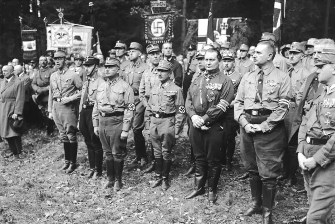Uroczystość z udziałem mężczyzn w mundurach, symbolizujących ideologię nazistowską i przekonanie o wyższości rasy aryjskiej.