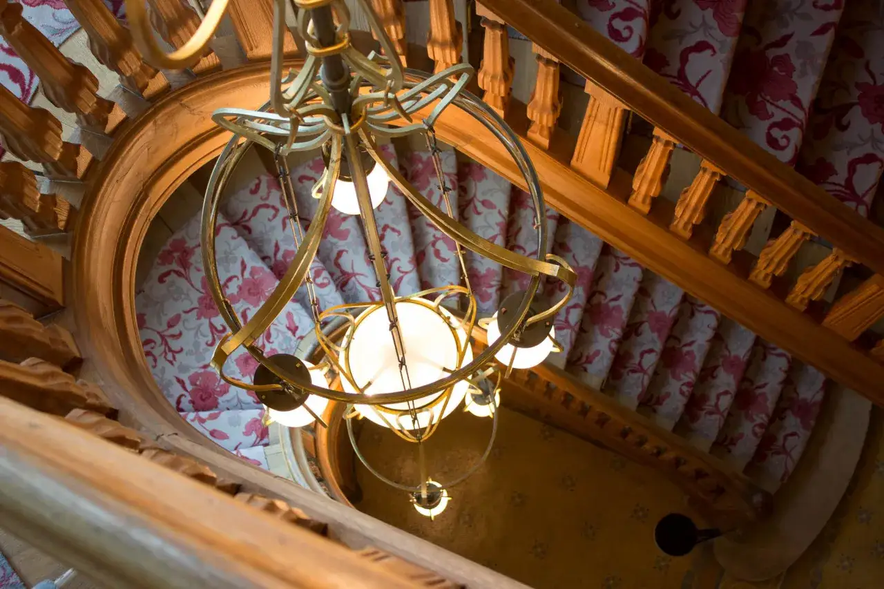 Lustre doré au-dessus d'un escalier en colimaçon avec tapis fleuri, évoquant le charme de la villa Demoiselle Pommery.