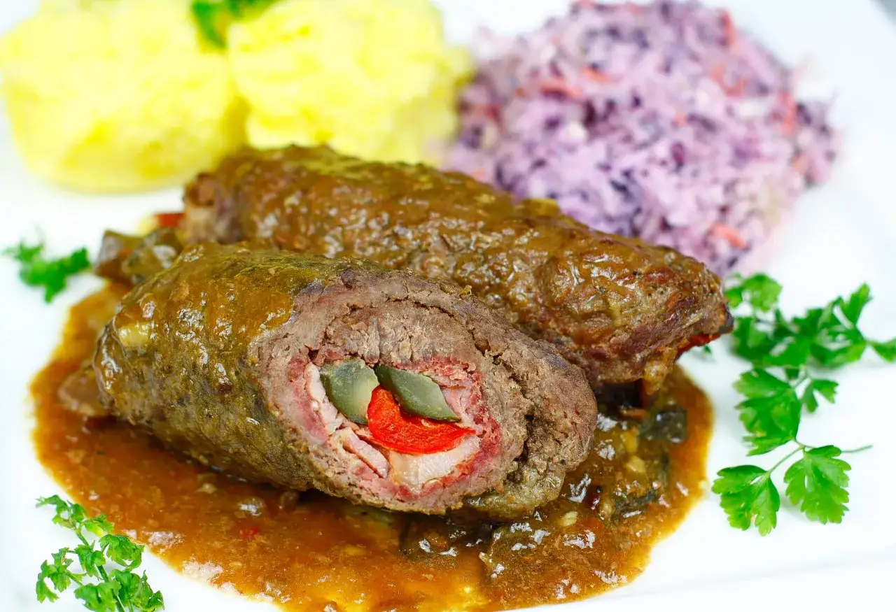 Pyszne rolady wołowe z piekarnika w sosie, podane z purée ziemniaczanym i surówką z czerwonej kapusty.