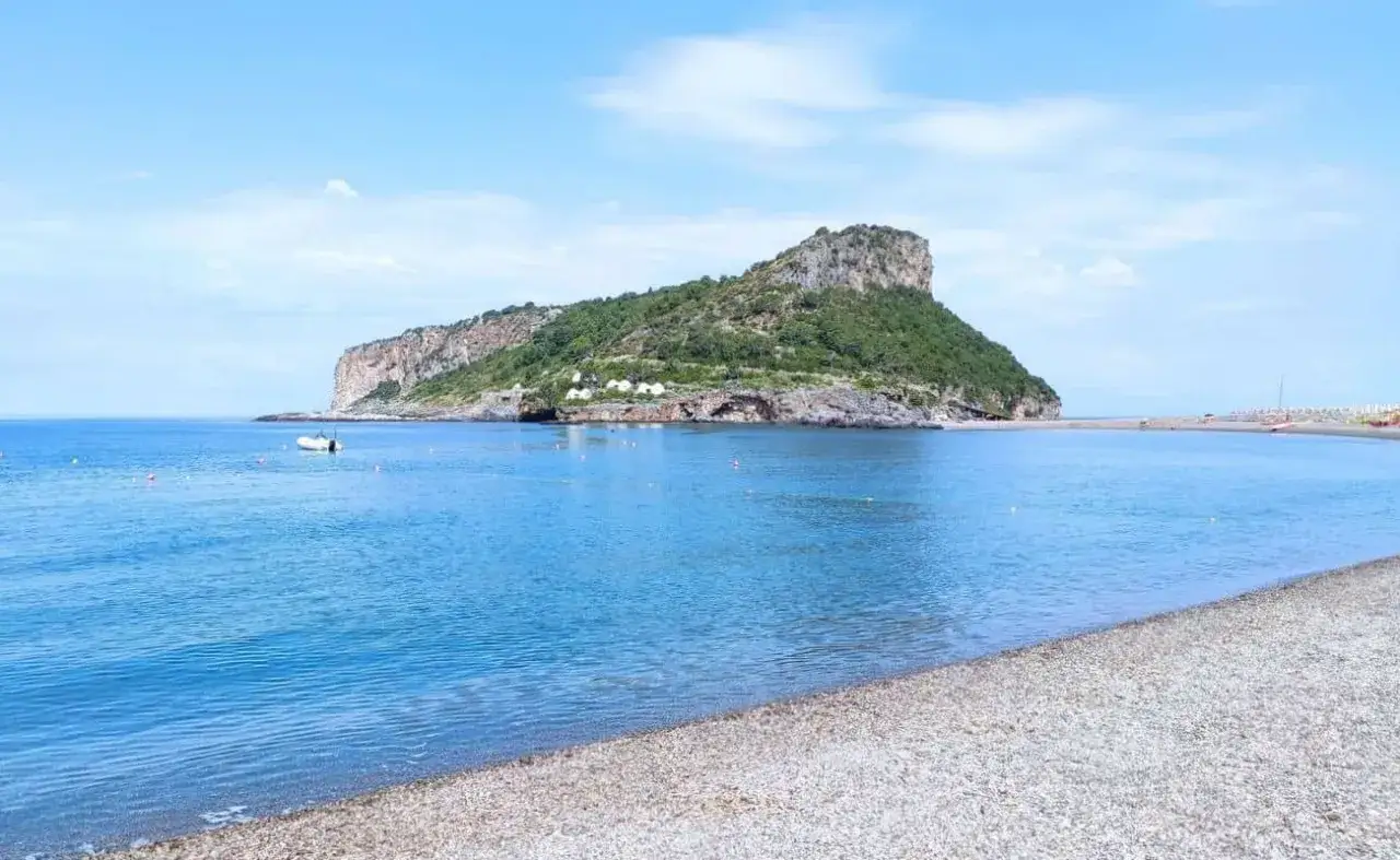 Spiaggia di ciottoli e mare azzurro nel **golfo di Policastro**, con un'isola verdeggiante sullo sfondo.