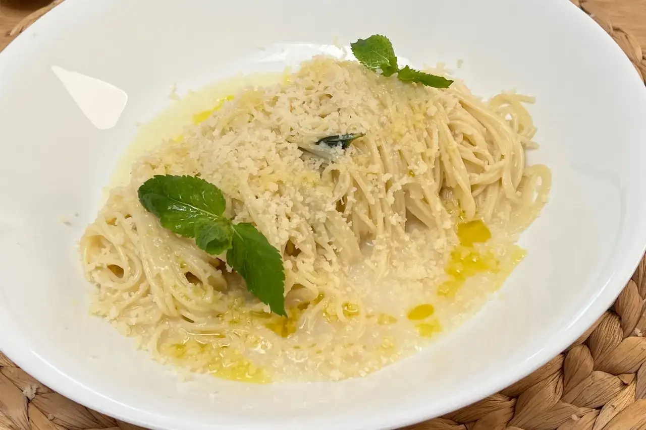 Spaghetti al limone cremosi, conditi con parmigiano e guarniti con menta fresca. Un piatto invitante e profumato.