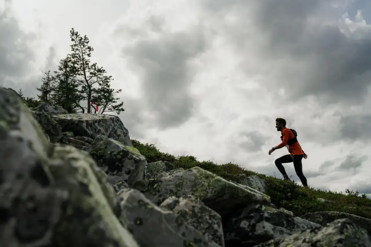 Un corredor asciende una ladera rocosa bajo un cielo nublado. Esto es trail running, pura aventura.
