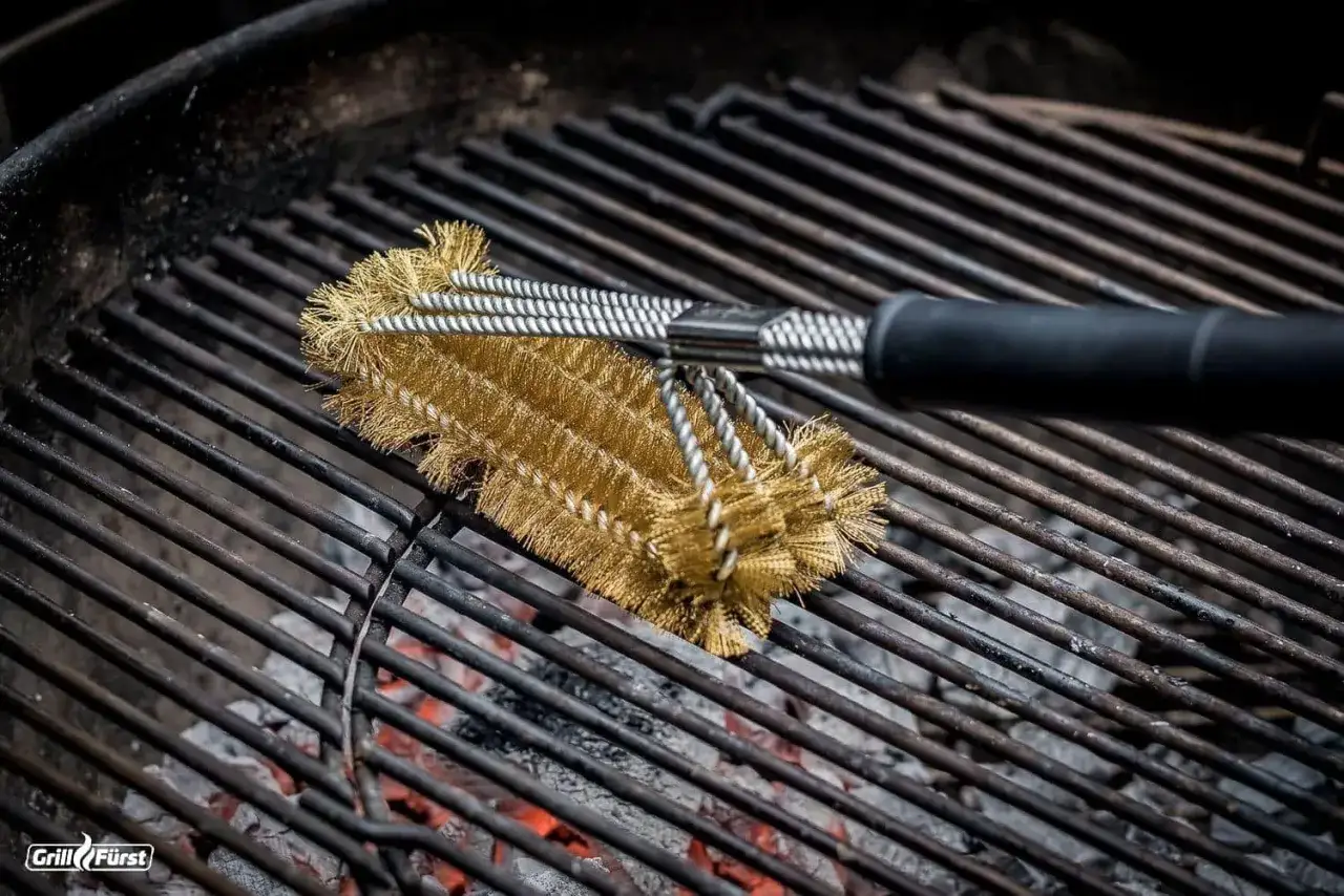 Grillbürste reinigt die alte Ofenplatte. Glühende Kohlen darunter.