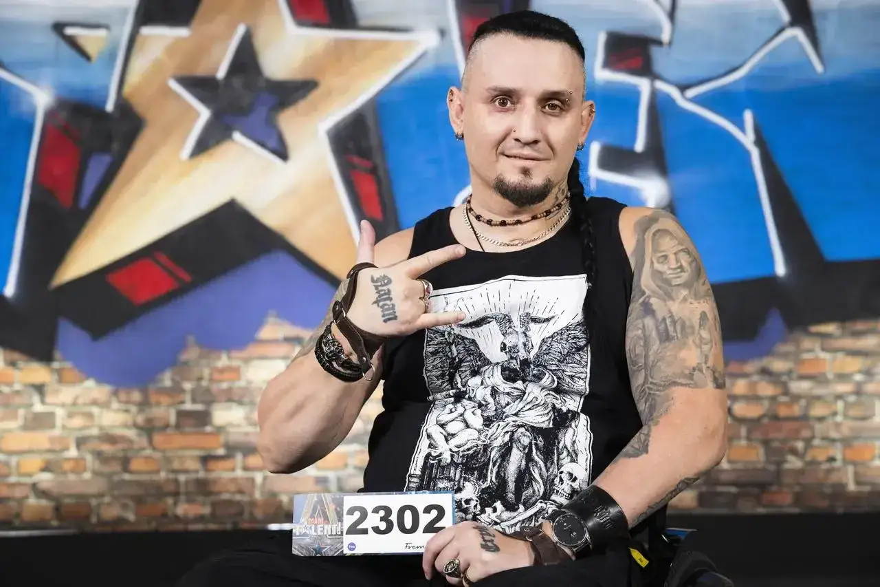 Tomasz Kowalski, muzyk z tatuażami i rockowym wizerunkiem, pozuje z gestem