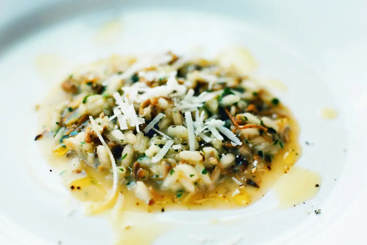 En kr&auml;mig, lyxig risotto med svamp och riven parmesanost, serverad p&aring; en vit tallrik.