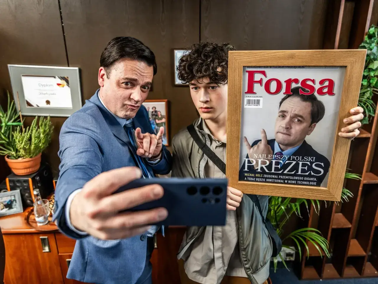Dw&oacute;ch mężczyzn w biurze, jeden robi selfie z ramką z okładką magazynu 