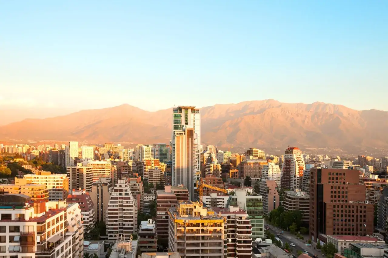Widok na nowoczesne budynki w Santiago de Chile o zachodzie słońca, z górami w tle.
