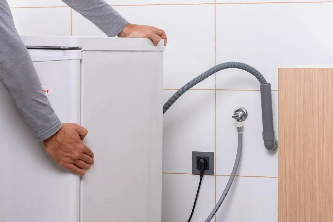 Hombre instalando lavadora, conectando manguera de desag&uuml;e a un tubo y enchufe.