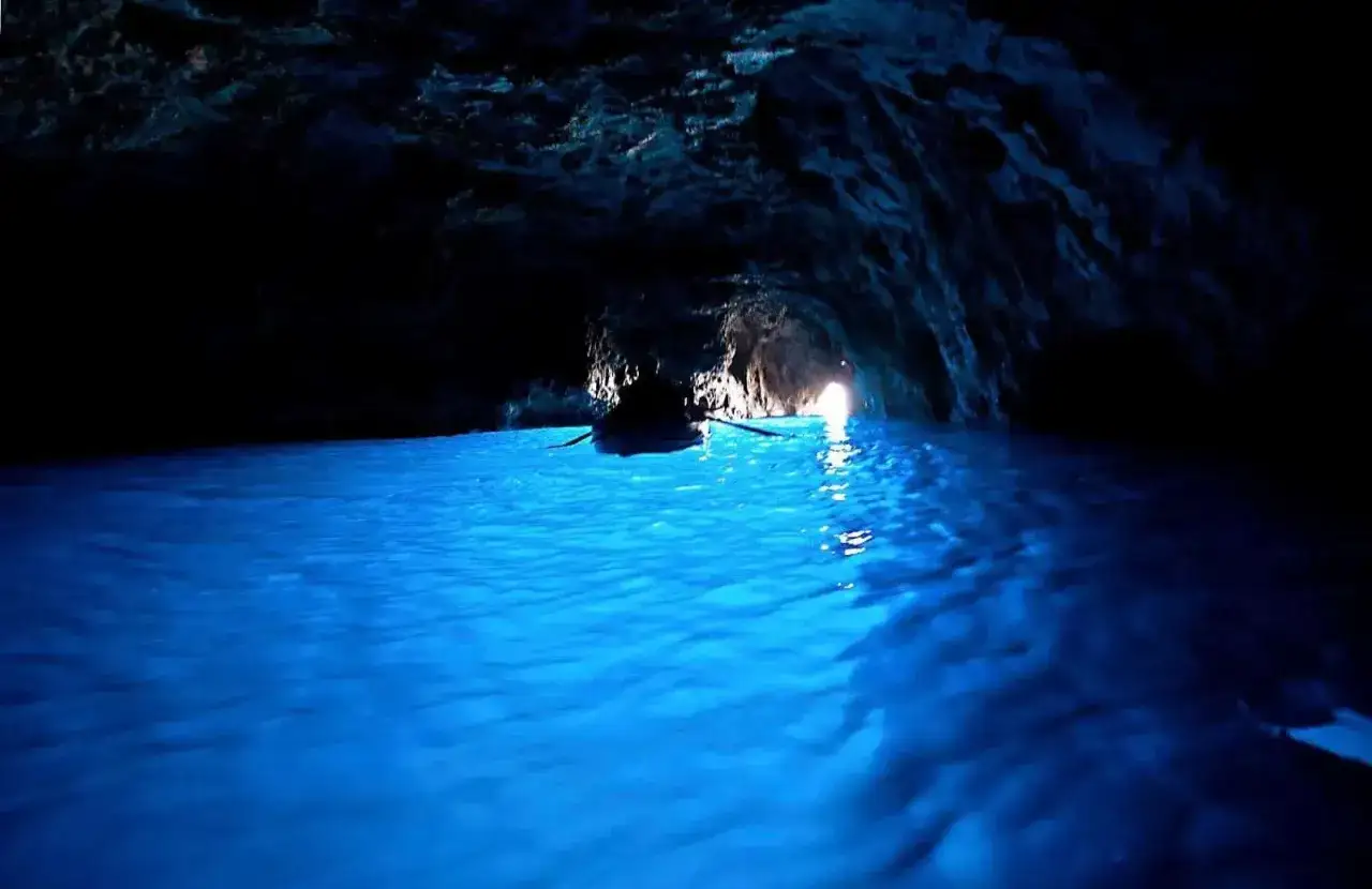 Barca a remi naviga nelle acque azzurre della grotta dello smeraldo, illuminata dalla luce che filtra dall'esterno.