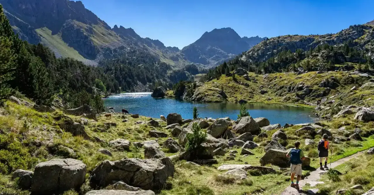 Deux randonneurs profitent d'une vue spectaculaire sur un lac bleu entour&eacute; de montagnes verdoyantes lors d'une randonn&eacute;e dans le Val d'Aran.