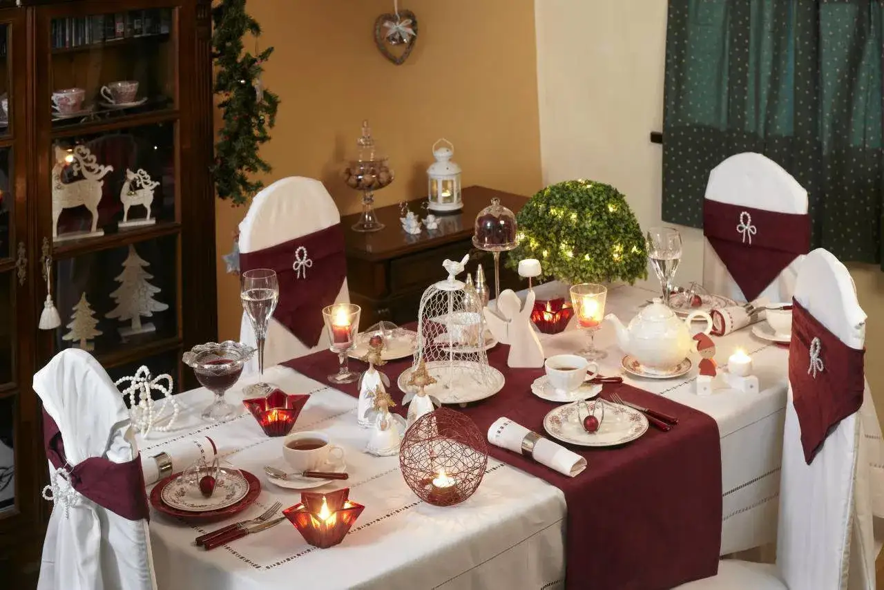 Elegancka wigilia w restauracji: stół nakryty białym obrusem, ozdobiony bordowym bieżnikiem, świecami, aniołkami i choinkowymi dekoracjami.