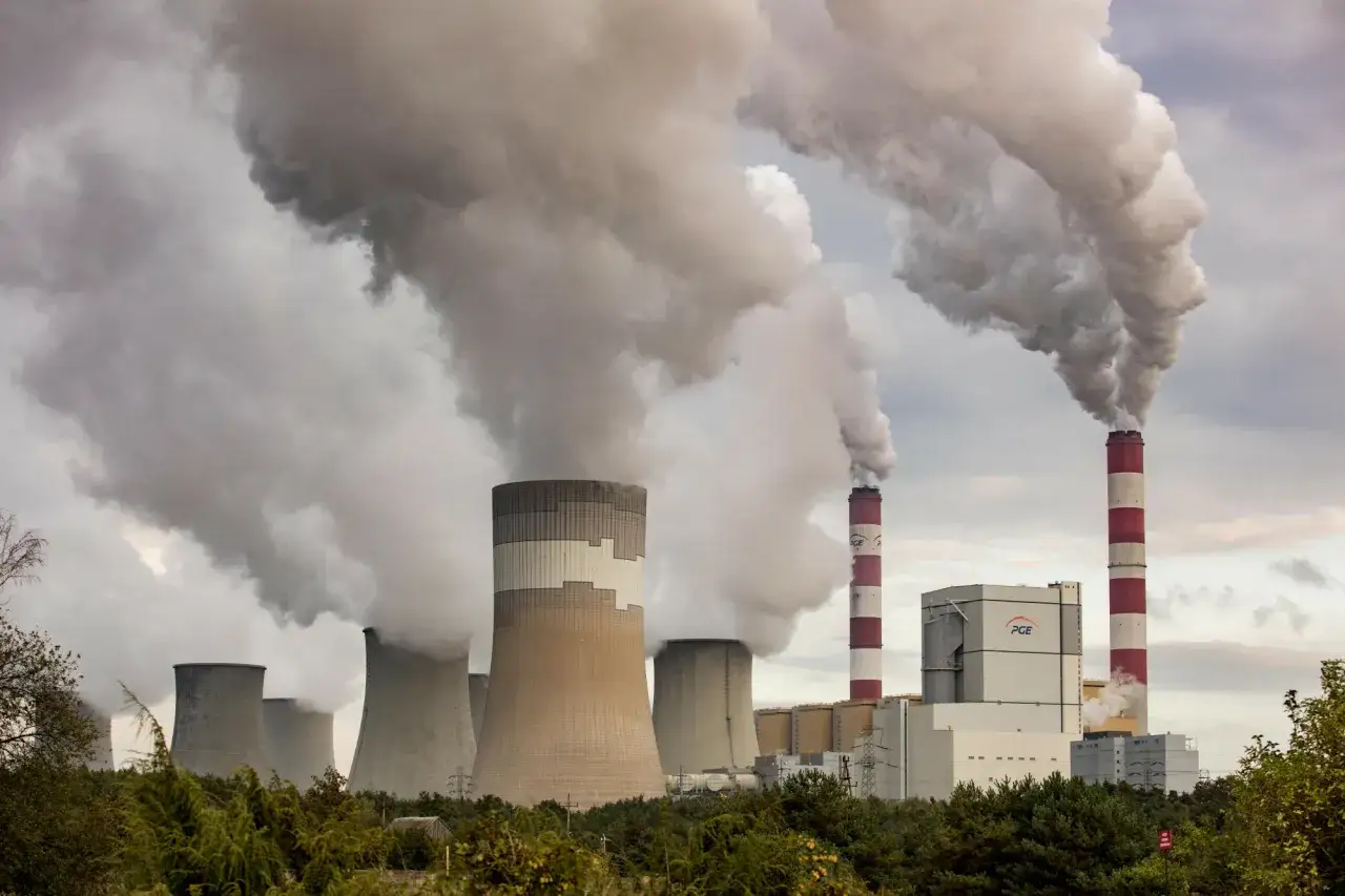 Ogromne chmury pary unoszą się z chłodni kominowych i dwóch czerwono-białych kominów elektrowni Bełchatów, pokazując, ile prądu produkuje elektrownia Bełchatów.