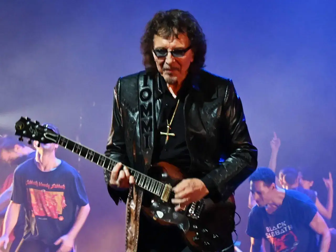 Tony Iommi, Gitarrist von Black Sabbath, spielt auf der B&uuml;hne. Fans im Publikum tragen Band-T-Shirts.