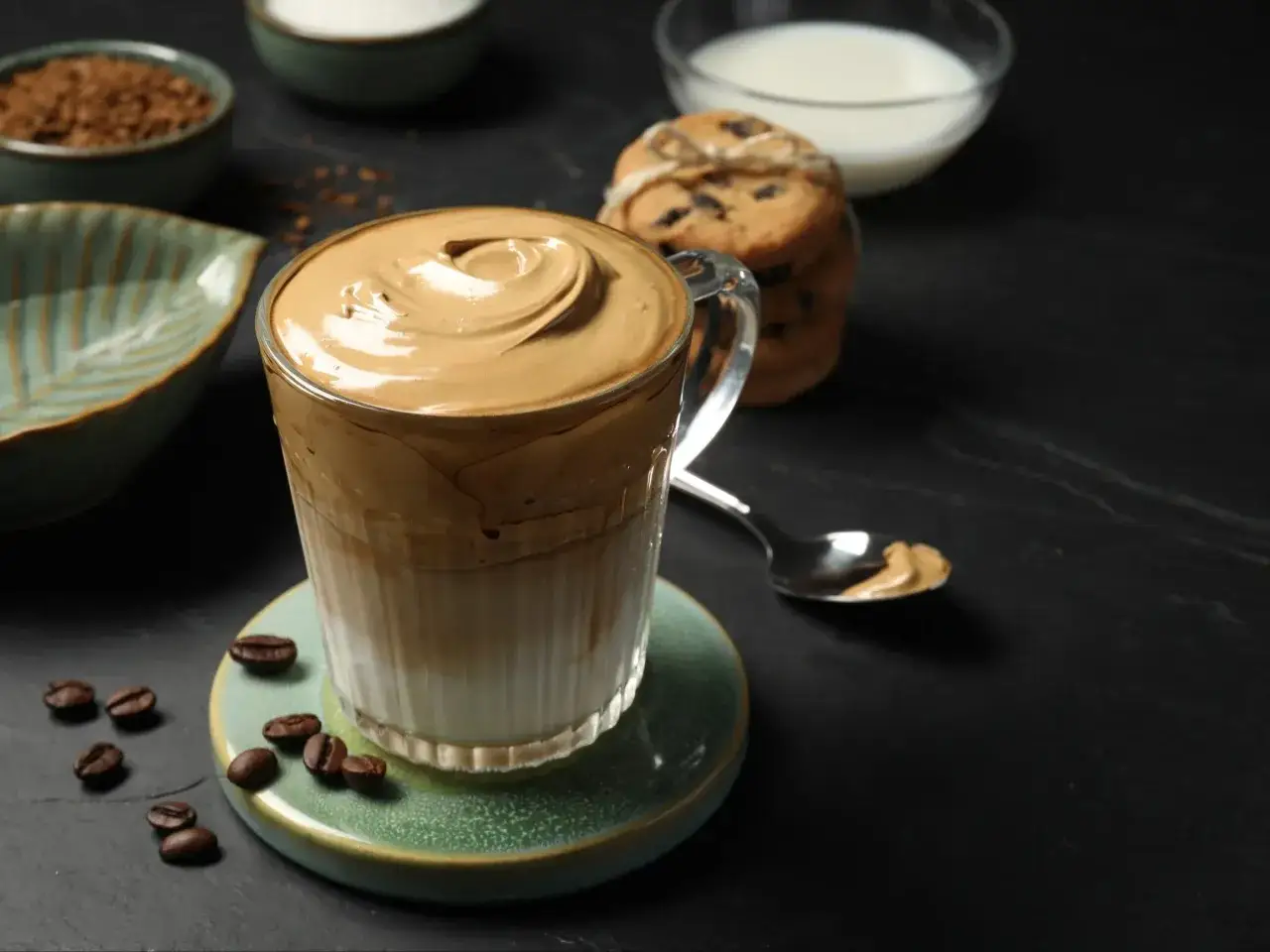 Puszysty, kremowy **dalgona coffee** w szklance, obok ciasteczka i ziarenka kawy. Idealny na chwilę relaksu.